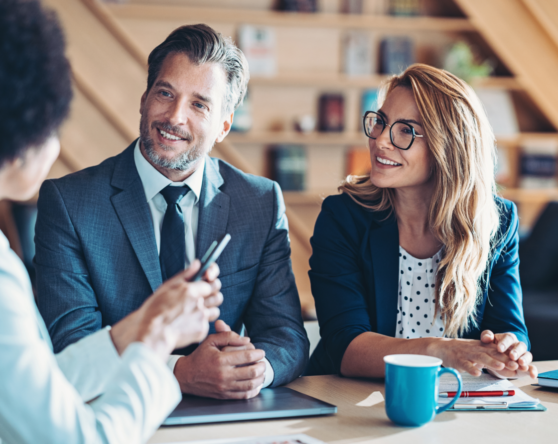zwei Frauen und ein Mann lächelnd bei einem Business Meeting